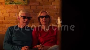 在舒适的公寓里坐在沙发上看3D电影的高级幸<strong>福</strong>夫妇的特写镜头